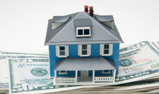 Picture of a home standing on a stack of saved money.